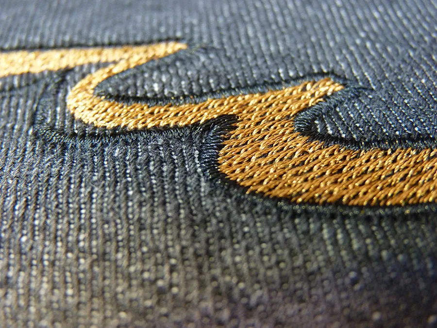 Close-up of a gold embroidered logo on dark fabric